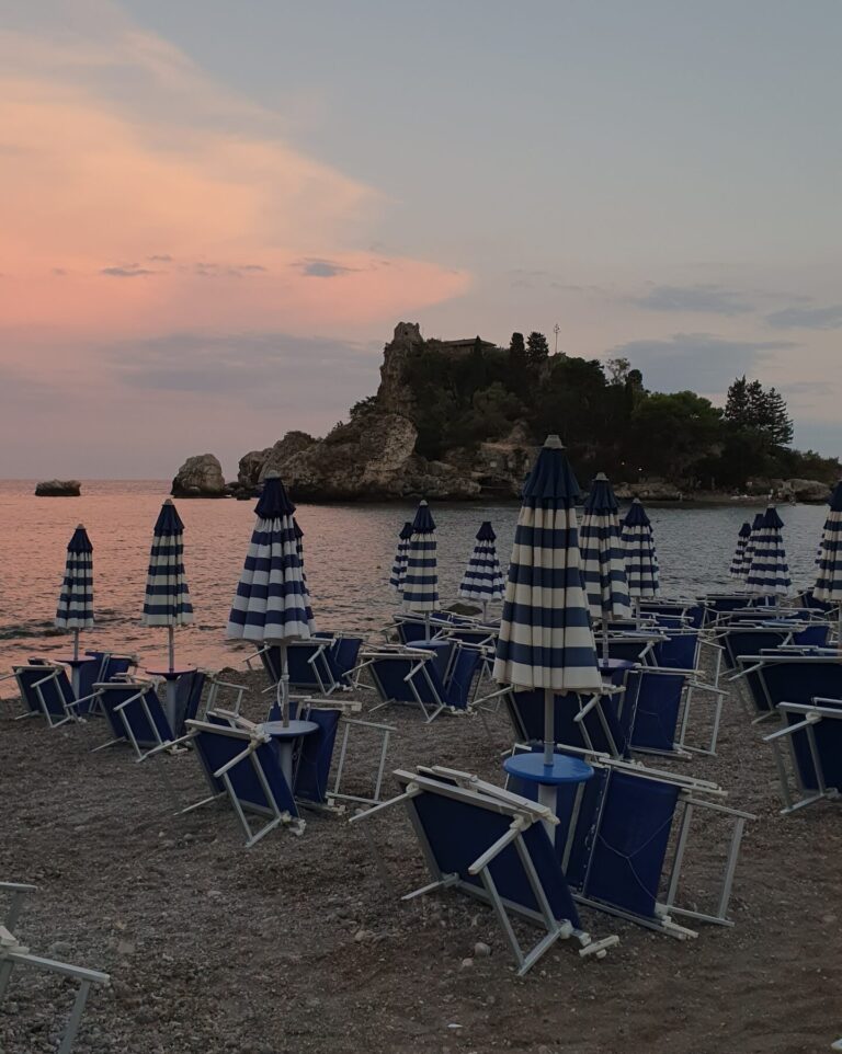 Sunset at Isola Bella in East Sicily. Beach with sun loungers and umbrellas.